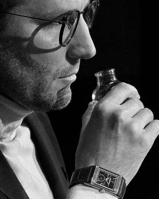 Dans le cadre de « Made of Makers » de Jaeger-LeCoultre, photo en noir et blanc de Nicolas Bonnevile en train de sentir un ingrédient pour mélanger un parfum, avec une Reverso Tribute Monoface Small Seconds à cadran noir au poignet, Q713257J