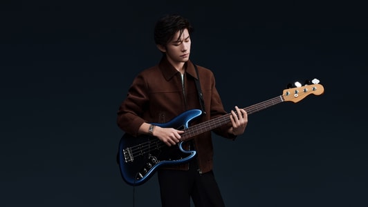 Jaeger-LeCoultre - Imagem de Jackson Yee vestindo uma jaqueta e tocando música Two Souls com um violão e usando um relógio Jaeger-LeCoultre Tribute Chronograph em ouro rosa em um fundo escuro - Q389257J